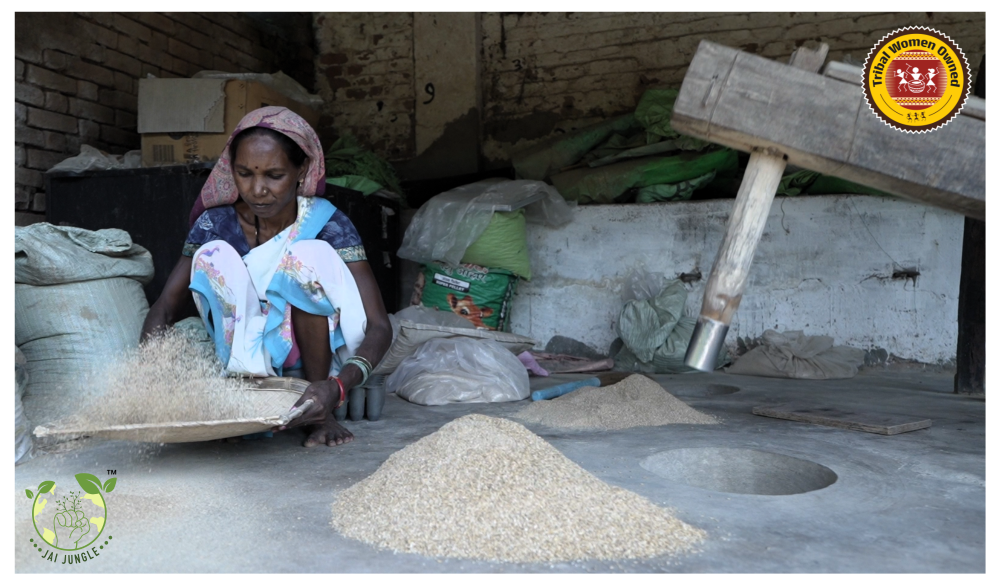 Tribal woman cleaning Javaphool rice by hand with traditional wooden Dheki pounding in the background – Jai Jungle women-led processing.